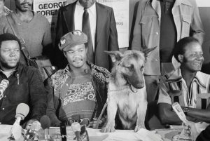 11 Sep 1974, Paris, France --- Original caption: 9/11/1974-Paris, France- Heavyweight champion George Foreman, accompanied by his dog, "Dago," answers newsmen's questions during a stopover at Orly Airport 9/11. Foreman is enroute for Kinshasa, Zaire, where he will defend his title, 9/25 against Muhammad Ali. "Dago" is shown looking at the camera. --- Image by © Bettmann/CORBIS